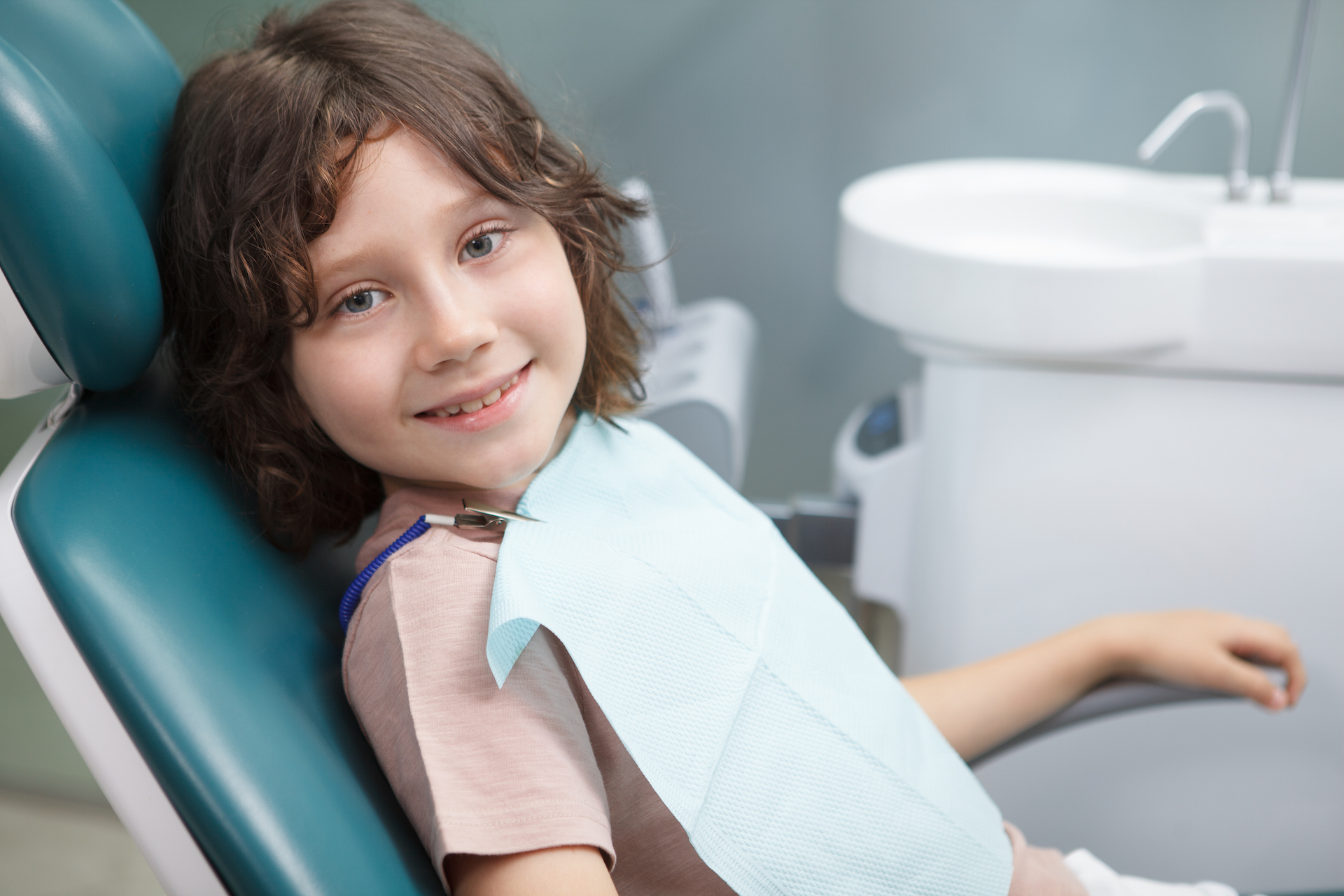 Lovely happy young boy smiling to the camera, sitting relaxed in dental chair