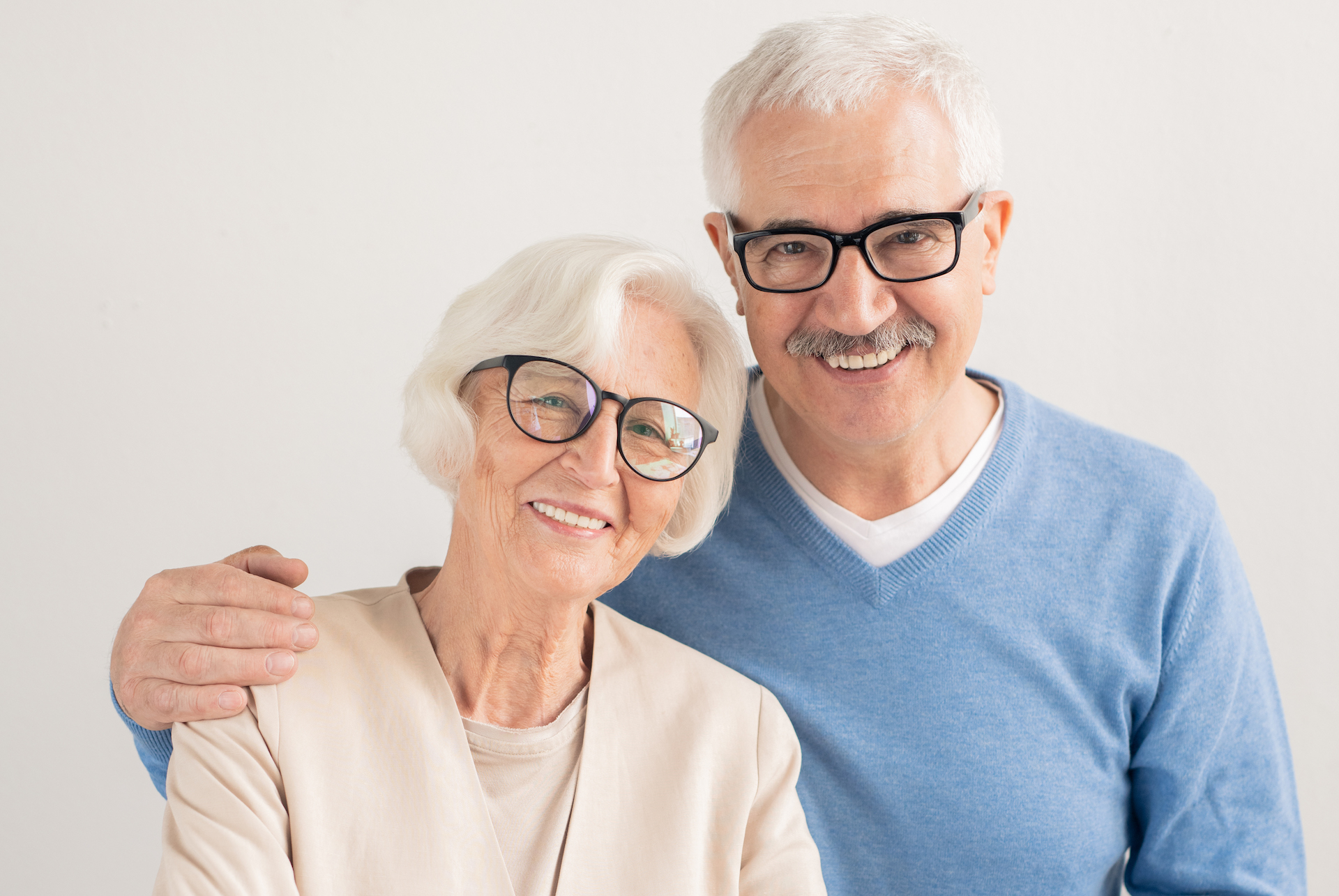 Happy senior affectionate couple with toothy smiles over white background standing in front of camera